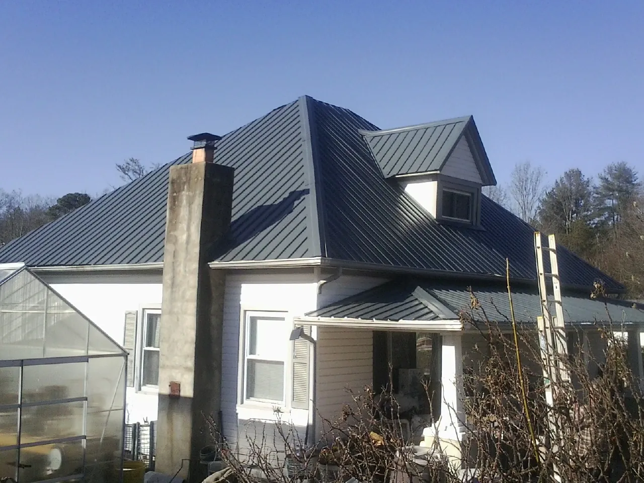 Dark blue standing seam metal roof on a white farmhouse with dormer — Slate & Tile Roof Repair by Roofing Brothers in Howard City