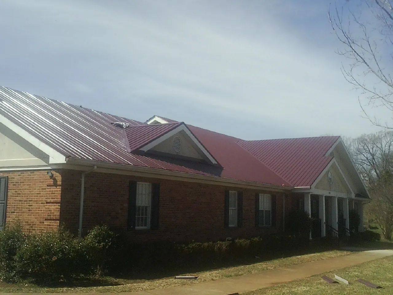 Red metal roof with gabled entries on a long brick building, from a Hail Damage Roof Repair job in Howard City