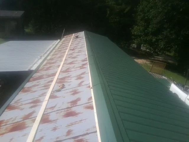 Old rusted panels beside newly installed green metal roofing — Wind Damage Roof Repair by Roofing Brothers in Howard City