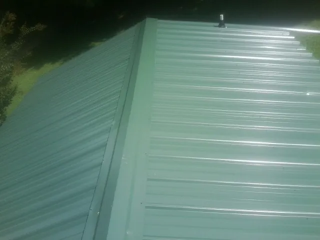 New green metal panels meeting at the ridge of a roof — Flat Roof Repair work by our crew in Howard City