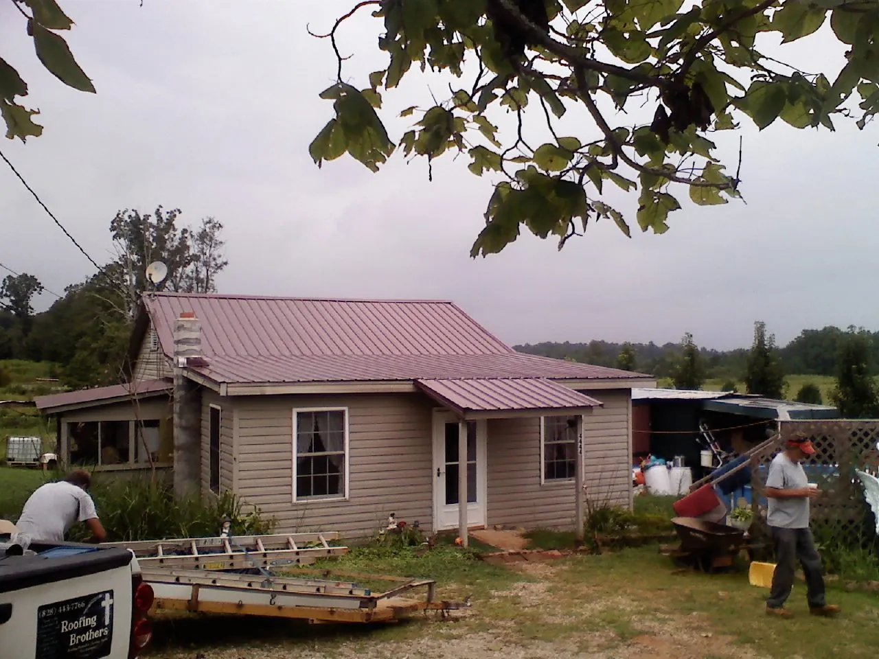 Crew finishing a mauve metal roof on a small farmhouse in Howard City