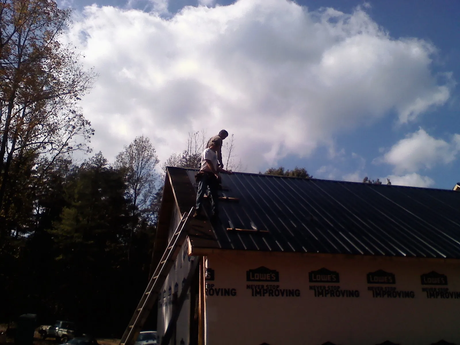 Roofer fastening dark metal panels high against a cloudy sky, from a Roof Inspection job in Howard City