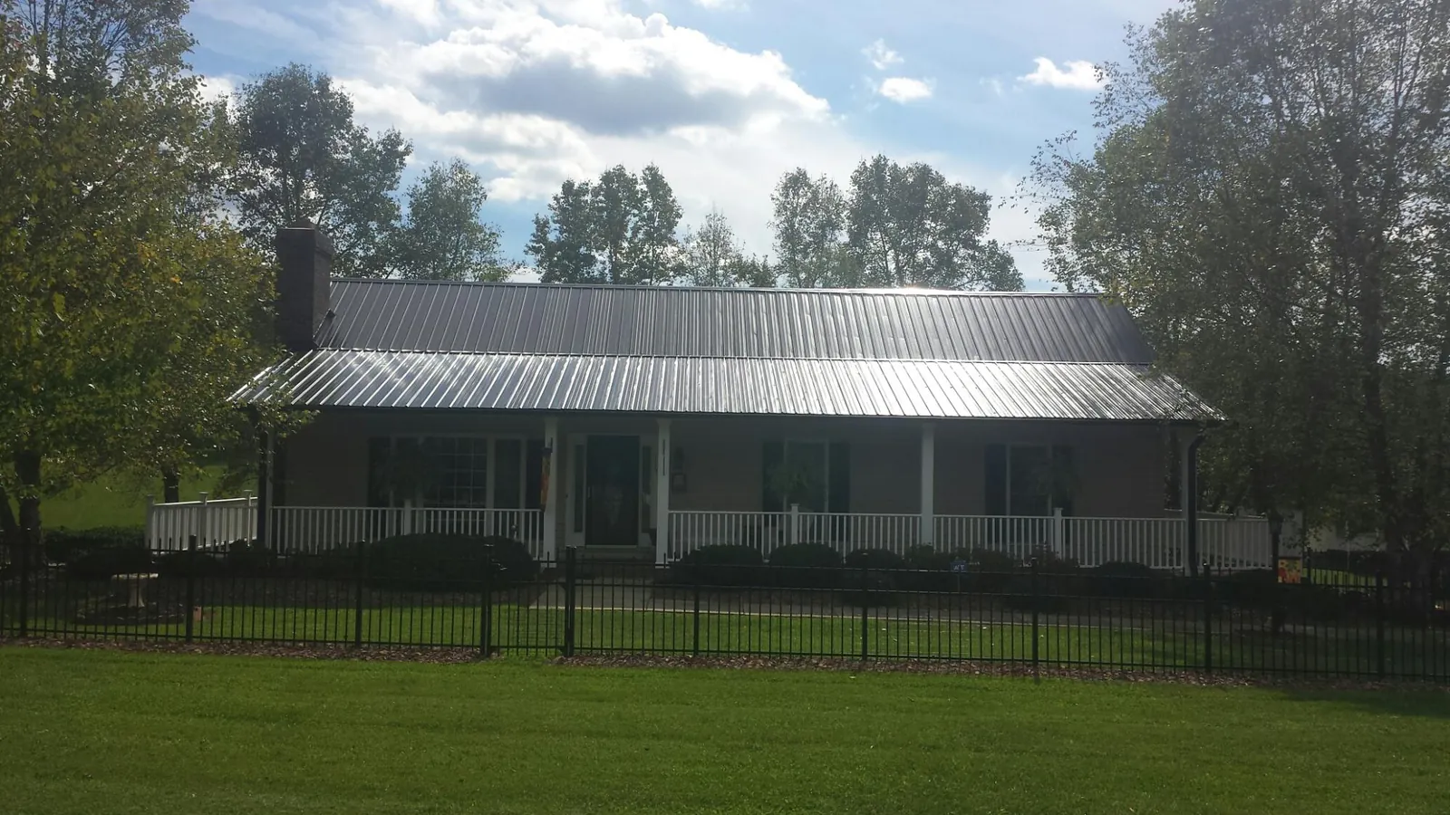 Gray metal roof on a brick ranch with a full width front porch — Gutter Guard Installation work by our crew in Howard City