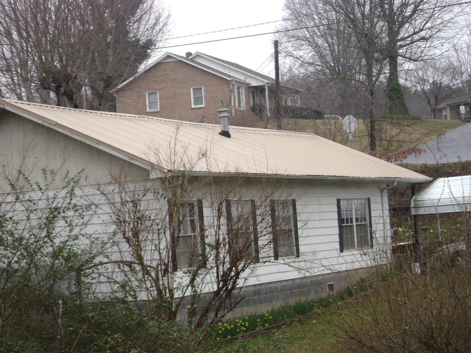 Tan metal roof on a white sided house set into a hillside — Commercial Roofing by Roofing Brothers in Howard City