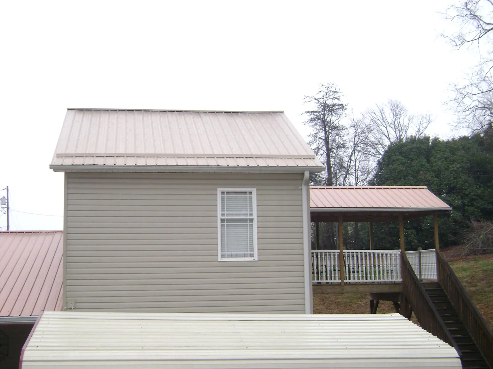 Tan metal roofs on a two story addition and attached porch, from a Roof Replacement job in Howard City