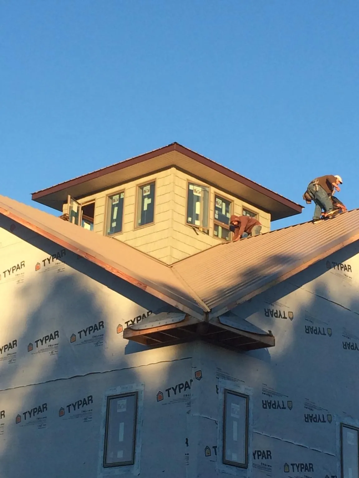 Roofers working around a rooftop cupola on a new metal roof at sunset — Roof Waterproofing in Howard City by Roofing Brothers